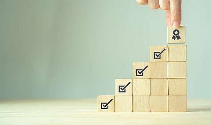 © 3rdtimeluckystudio / Shutterstock.com Eine Treppe aus Holzwürfeln, 2 Finger setzen gerade den obersten Würfel auf