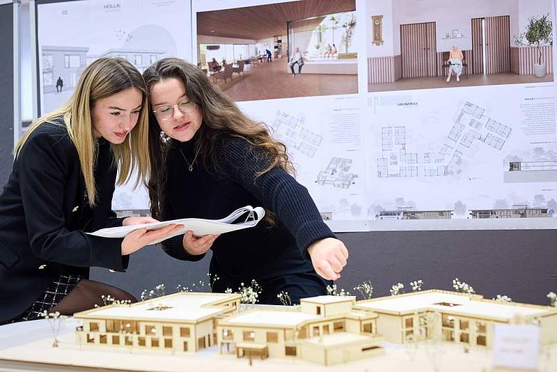 © HCW / Schedl 2 Personen zeigen auf und sprechen über ein Architektur Modell