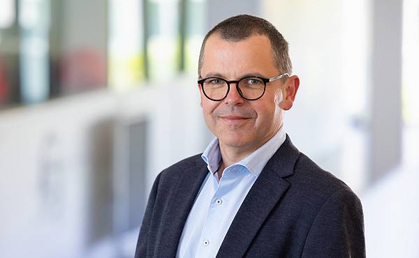 © HCW/Schedl Portrait von einem Mann mit kurzem braunen Haar in einem hellblauen Hemd mit dunklem Sacko im Gang des Hauptgebäudes