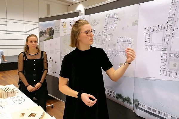 Zwei Studierende erläutern ihre Entwürfe vor Plakatwand