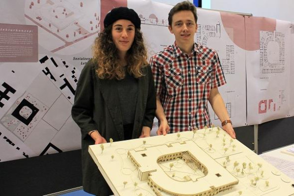 Studierende und Studierender halten gemeinsam Holzmodell vor Wand mit architektonischen Plakaten