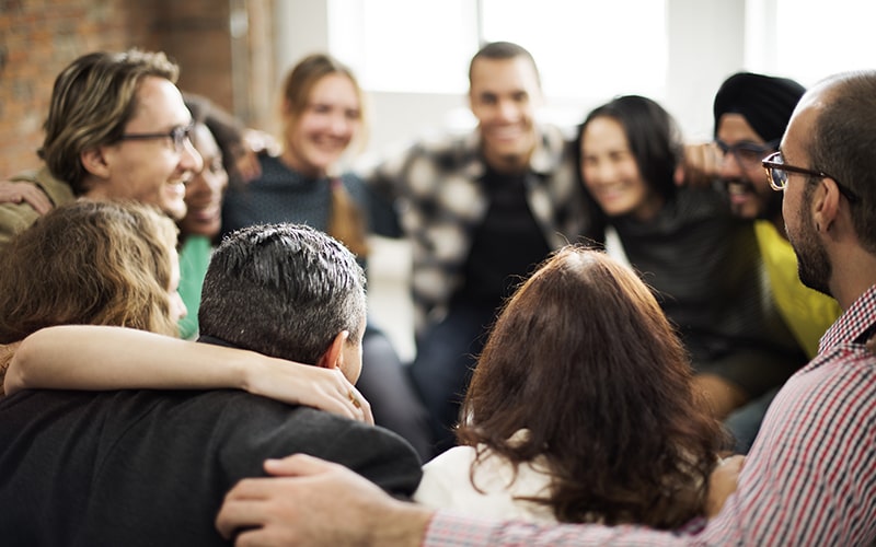 © shutterstock/rawpixel.com Eine Gruppe von Personen steht in einem Kreis und hält sich an den Schultern