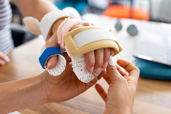 © HCW/Schedl Zwei Hände, eine Hand ist in einer Schiene.