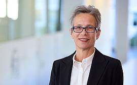 © HCW/Schedl Portrait einer Dame mit kurzem Haar und Brille in weißer Bluse und dunkelblauem Blazer vor Besprechungstisch