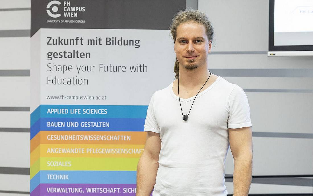 © HCW / Dujmic Einer der StartUp-Gründer*innen steht vor einem Banner der Hochschule Campus Wien