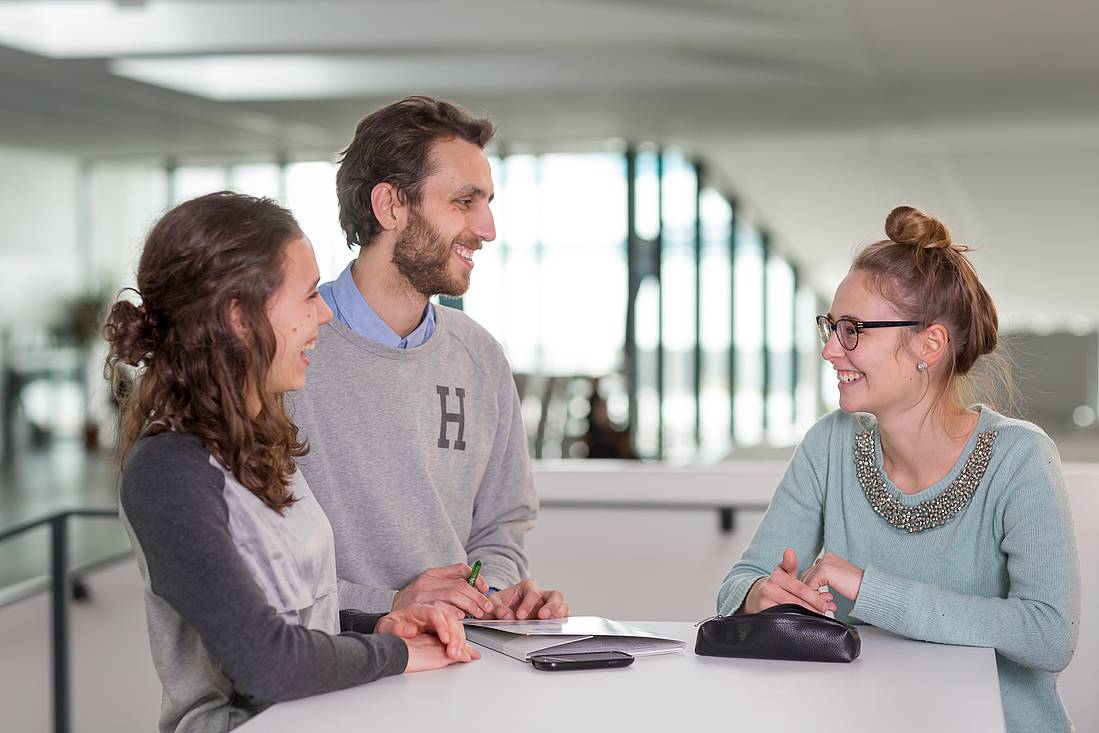 Two women and a man standing around a table and conversing