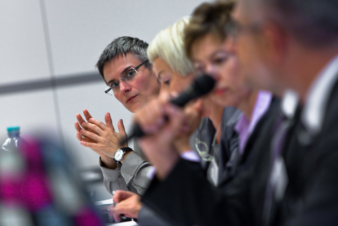 Vier Personen von der Seite abgebildet, sitzen an einem Tisch.