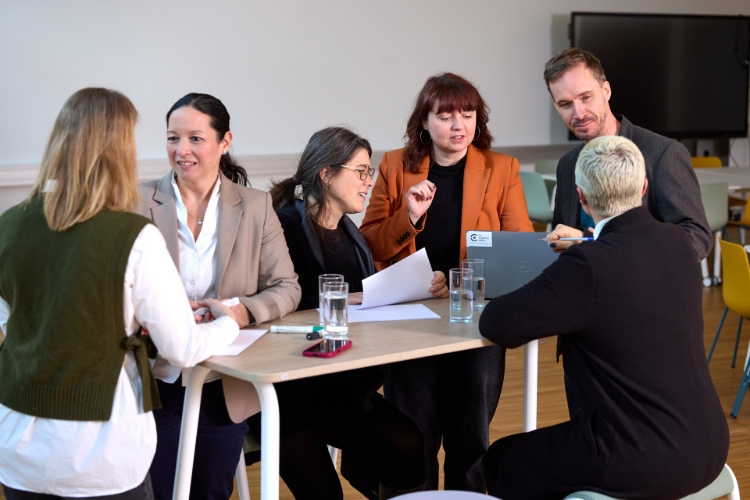© HCW/Schedl Gruppe von Erwachsenen sitzt an einem Tisch und bespricht Unterlagen