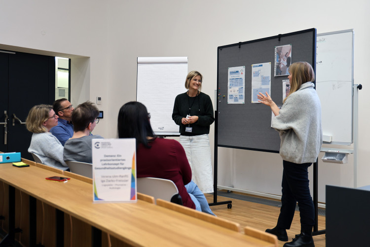 © Hochschule Campus Wien/Christl Eine Gruppe von Leuten diskutiert vor einer Pinnwand, auf der Dokumente hängen.